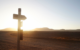 An image of a barren road with a street sign that looks like a cross, pointing the way.